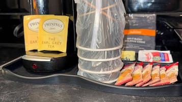 Een koffiezetapparaat, een plastic bak en een dienblad met theezakjes en snacks op een aanrecht.