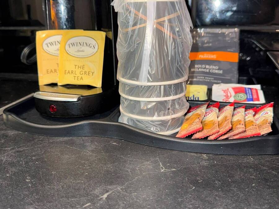 Een koffiezetapparaat, een plastic bak en een dienblad met theezakjes en snacks op een aanrecht.