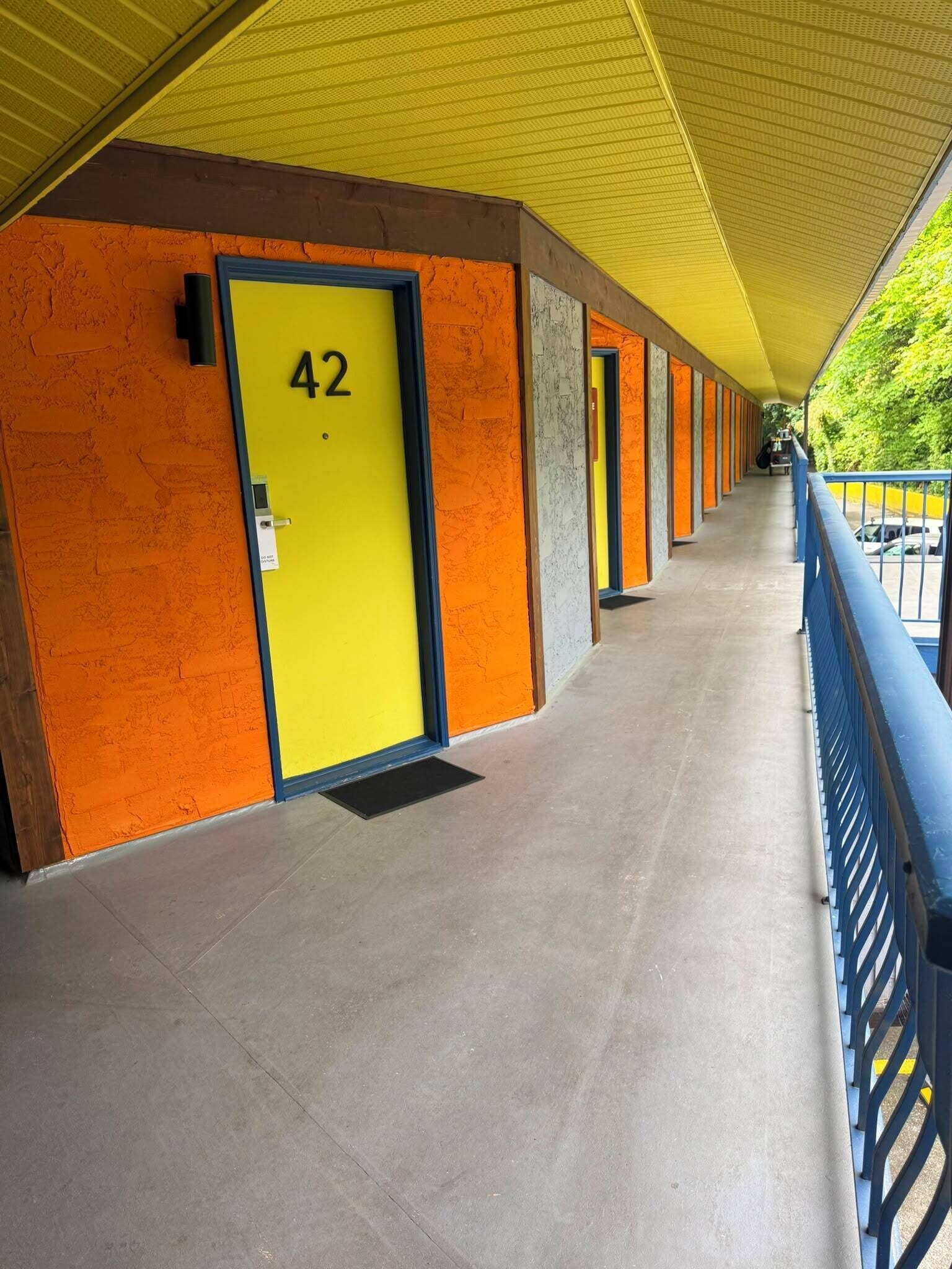 A corridor with a yellow door marked '42', a metal railing, and a tiled floor.