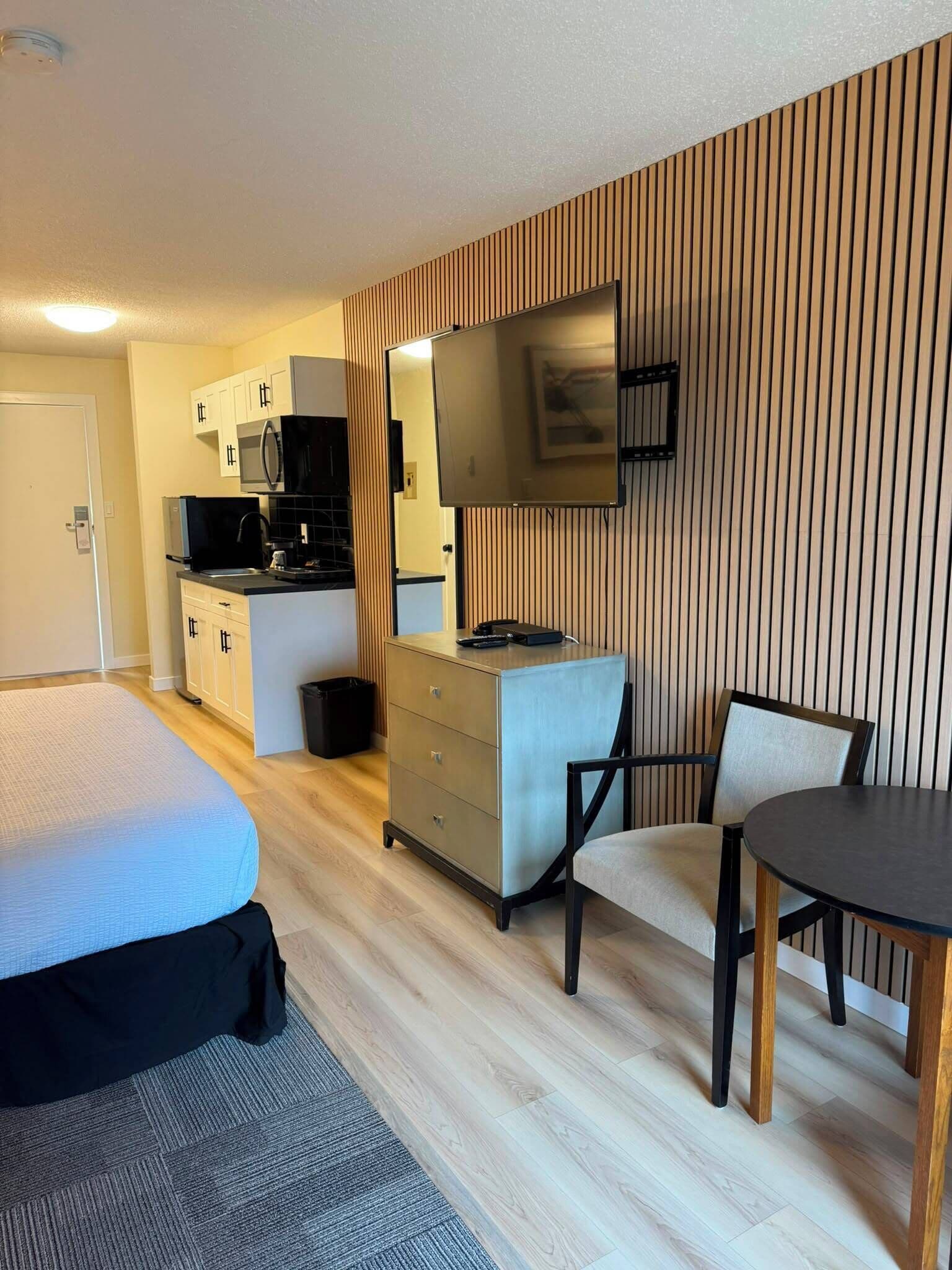 Habitación de hotel con cama, escritorio con silla, kitchenette y un espejo grande.