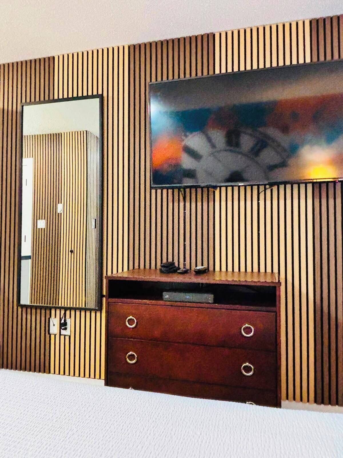 Une pièce avec un mur lambrissé, un grand téléviseur à écran plat, un miroir et un meuble en bois doté de tiroirs.