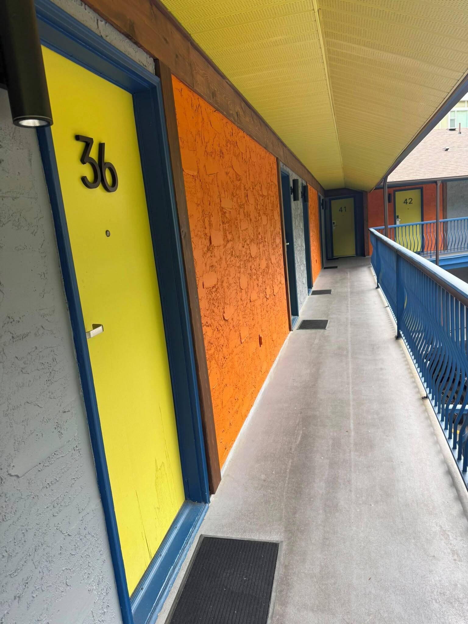 Un pasillo con puertas numeradas 36 y 42, una barandilla azul y un techo amarillo.