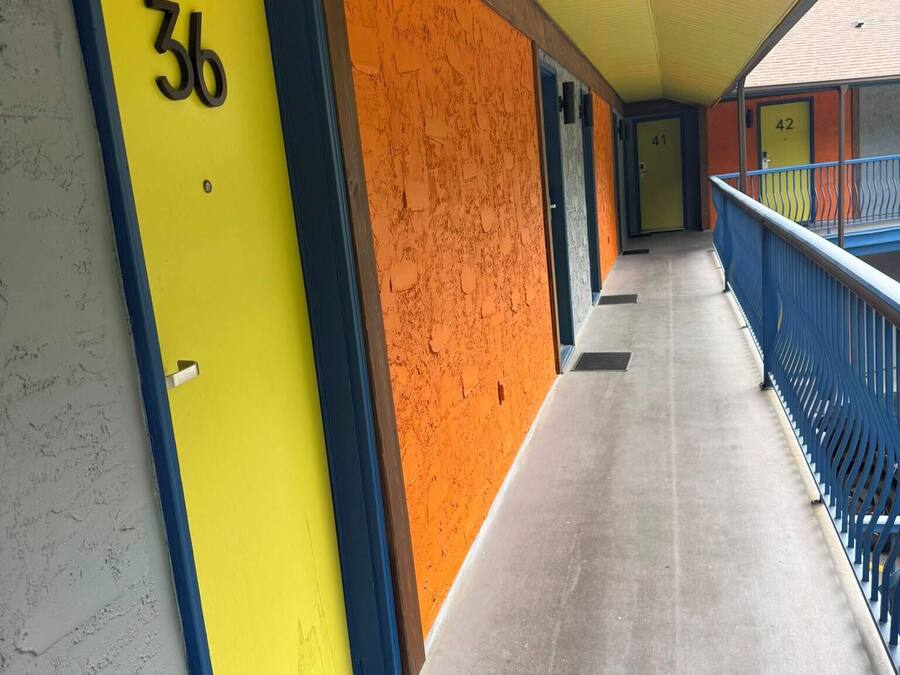 Un pasillo con puertas numeradas 36 y 42, una barandilla azul y un techo amarillo.