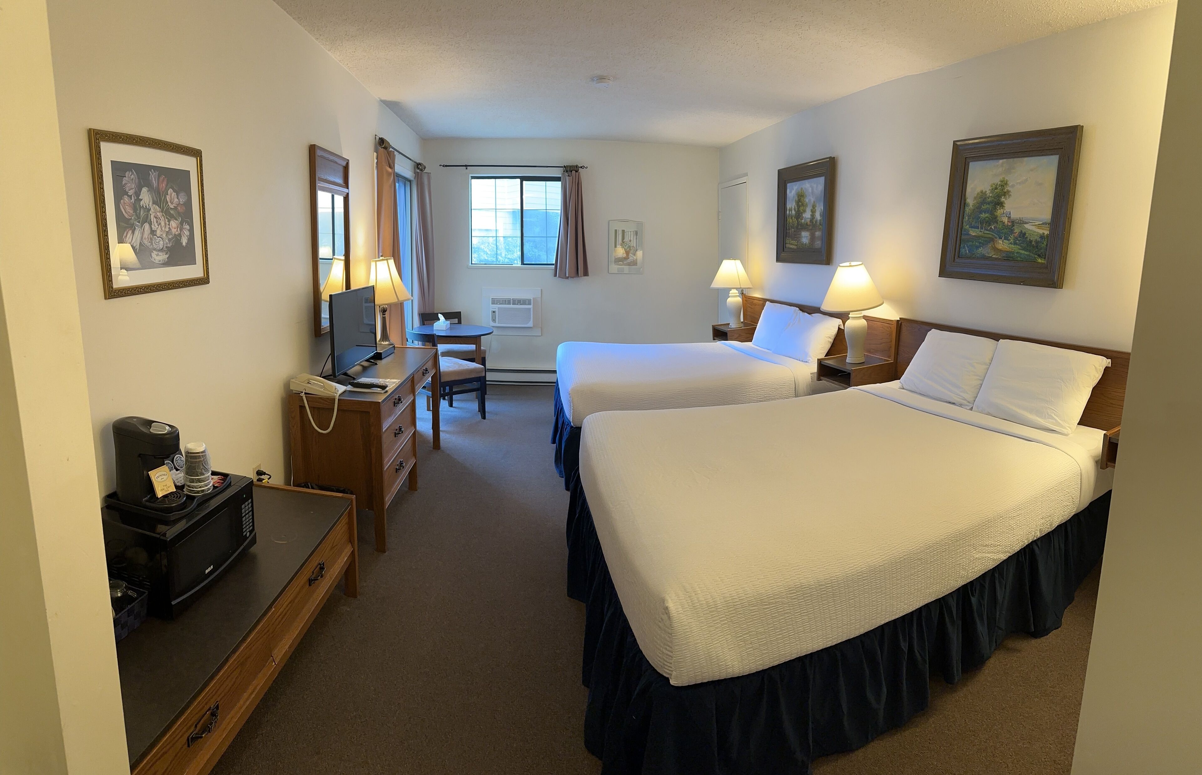 A hotel room with two beds, a desk, a chair, a coffee maker, and a microwave.