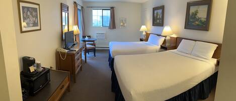 A hotel room with two beds, a desk, a chair, a coffee maker, and a microwave.