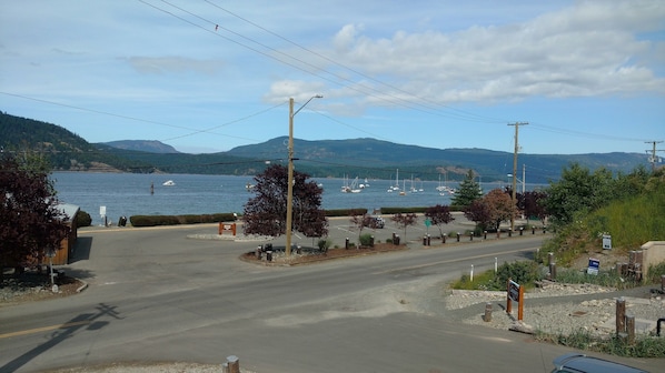 A coastal road with a parking area, a sign for a campground, and a view of the sea with boats.