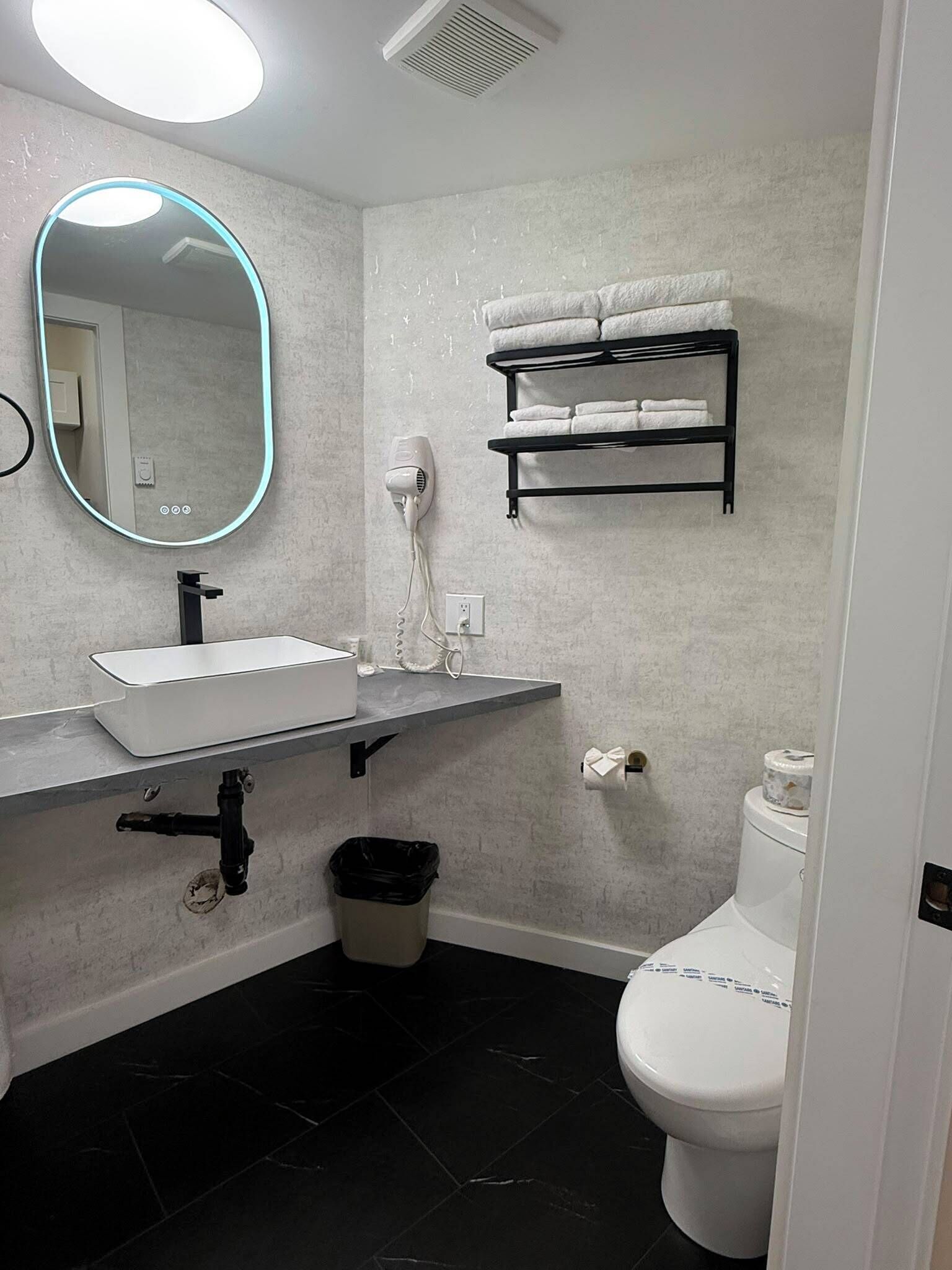 Une salle de bain avec un lavabo blanc, un miroir, un sèche-cheveux, un porte-serviettes et des toilettes.