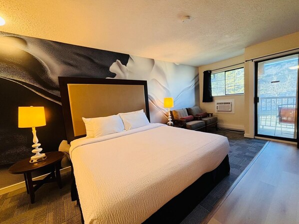 A hotel room with a large bed, a nightstand, a chair, a sofa, a window, and a wall mural. - Wessex Inn By The Sea (Cowichan Bay)