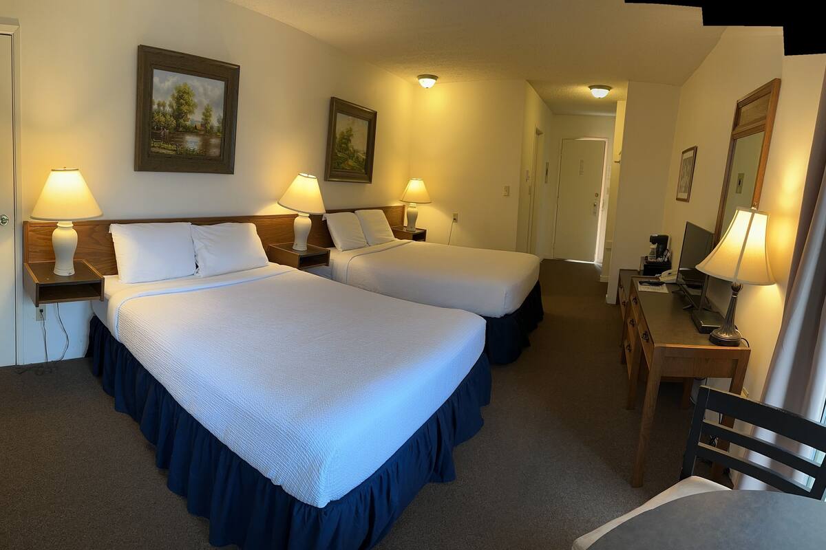 Ein Hotelzimmer mit zwei Betten, Nachttischen mit Lampen, einem Schreibtisch und einem Stuhl sowie einer Tür.