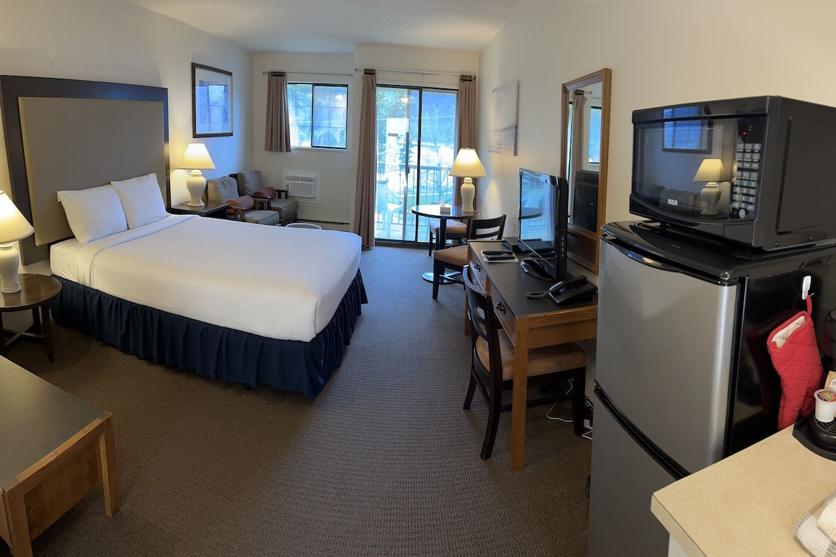 Ein Hotelzimmer mit Bett, Schreibtisch, Fernseher, Kühlschrank und einem kleinen Esstisch.