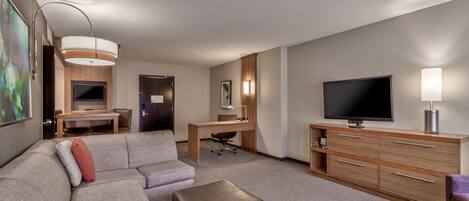 Habitación de hotel con sofá modular, una mesita, un escritorio con silla, televisor y un armario.
