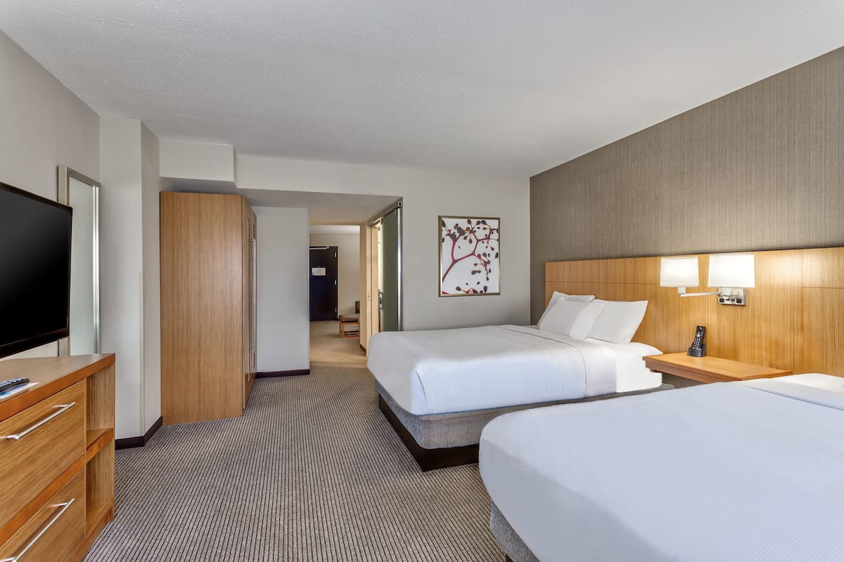 Een hotelkamer met twee bedden, een televisie, een houten garderobe, een ingelijst kunstwerk en een nachtkastje met een lamp.