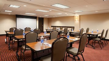 Sala de conferência com várias mesas e cadeiras, equipada com garrafas de água e papéis.