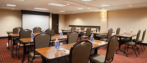 A conference room with multiple tables and chairs, equipped with water bottles and papers.