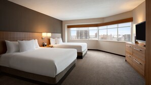 A hotel room with two beds, a large window with a city view, a flat-screen TV, and a wooden dresser.