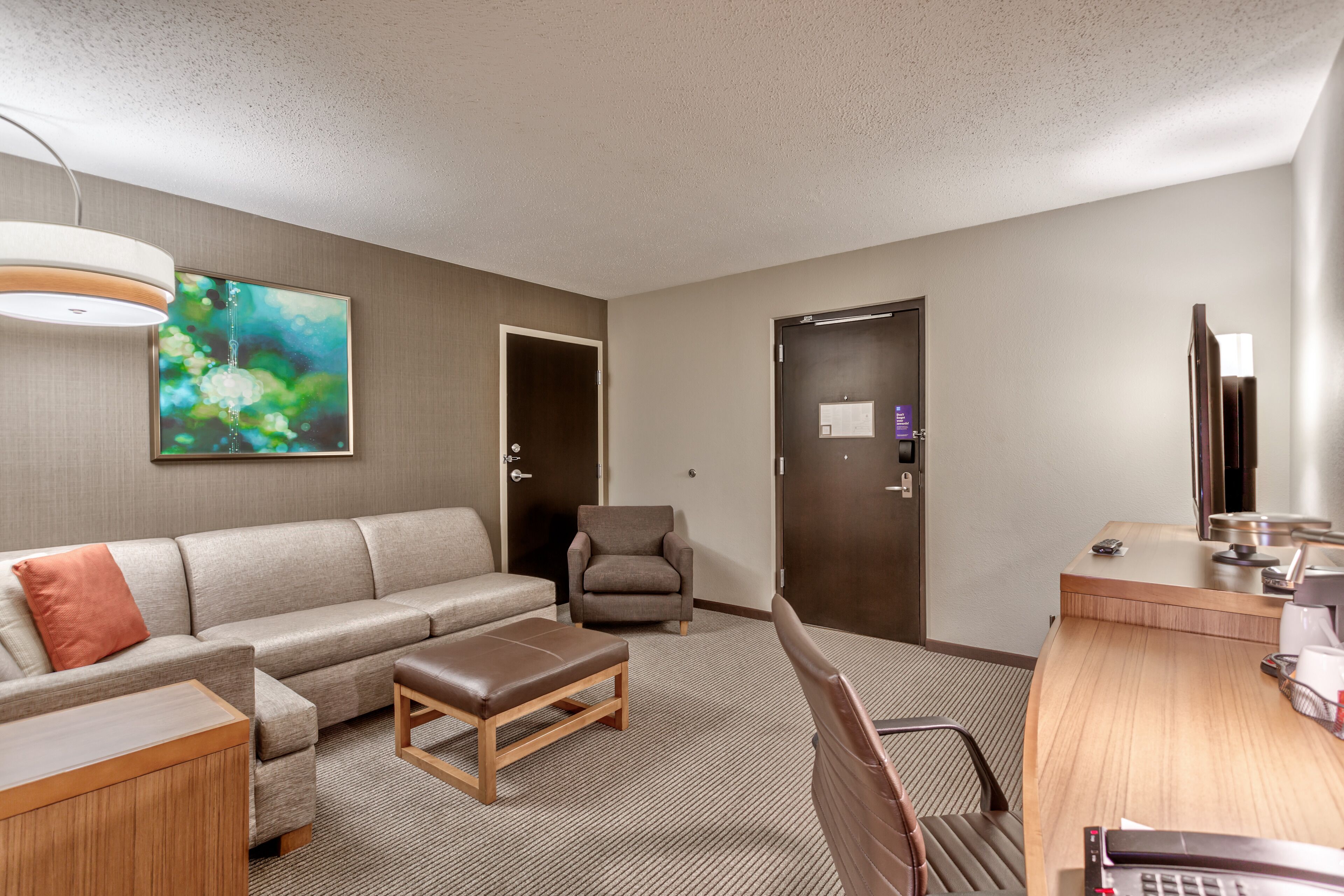 Quarto de hotel com sofá, poltrona, escrivaninha e um quadro na parede.