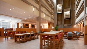 A spacious indoor area with multiple wooden tables and chairs, a large window, and a staircase leading to an upper level.