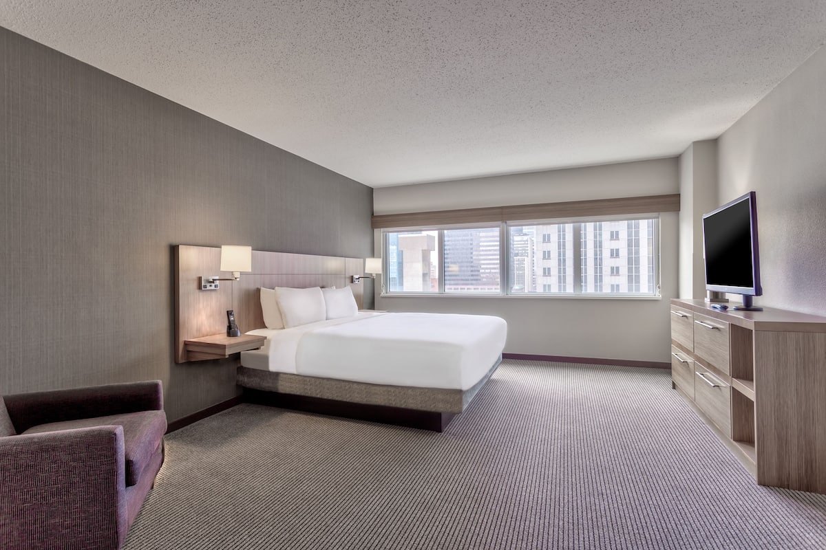 Een hotelkamer met een groot bed, een televisie, een bureau met lamp en uitzicht op de stad.
