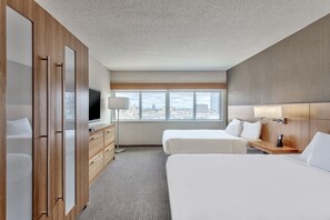 Une chambre d’hôtel avec deux lits, une télévision, un bureau avec une lampe et une vue sur la ville grâce à de grandes fenêtres.
