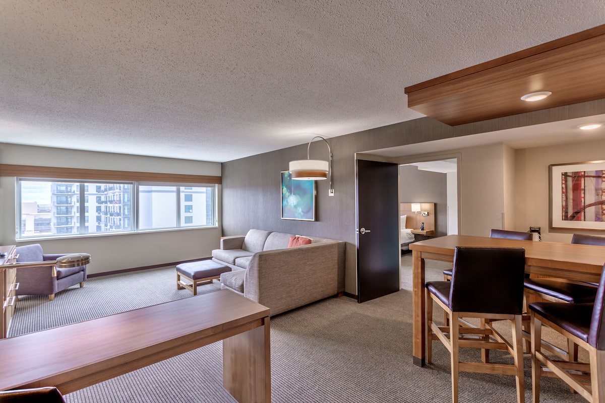 Een moderne hotelkamer met een groot raam, een bank, een eettafel en een houten plafond.