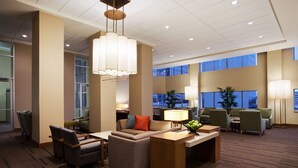 A modern hotel lobby with a seating area, a reception desk, and large windows.