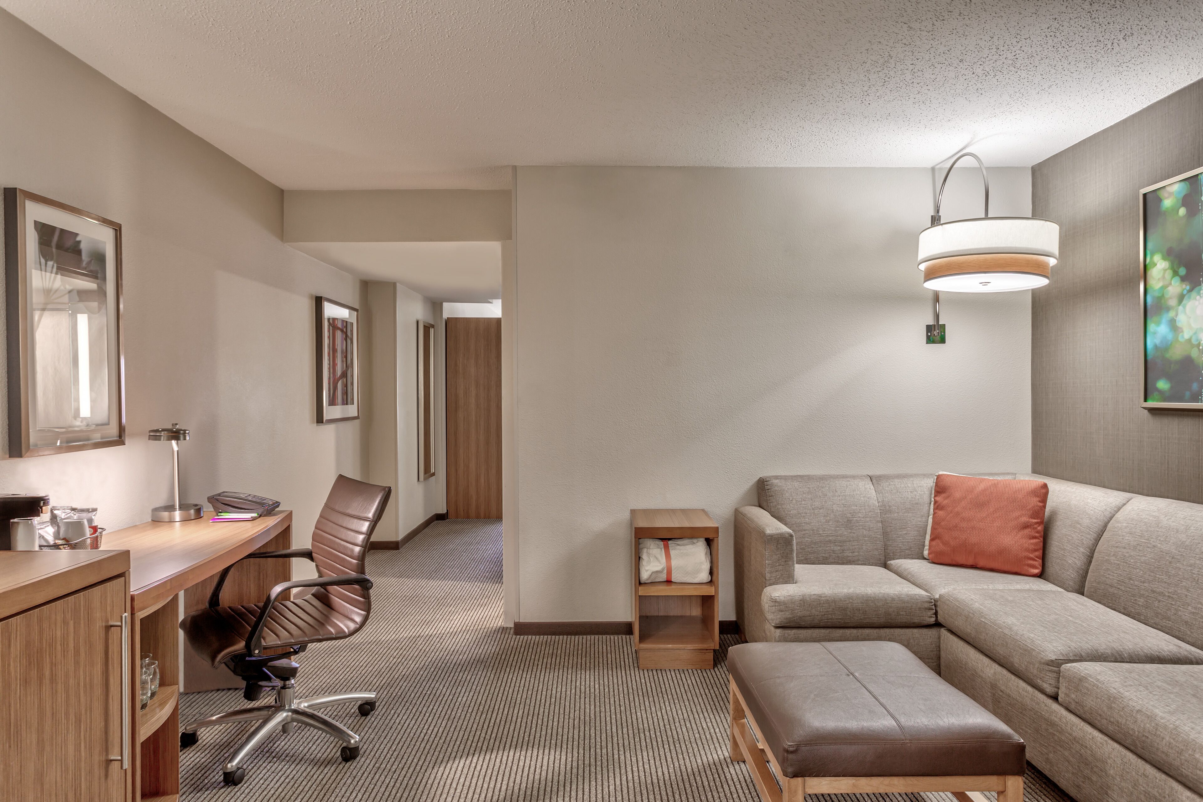Een moderne hotelkamer met een houten bureau, bureaustoel, bank en poef.