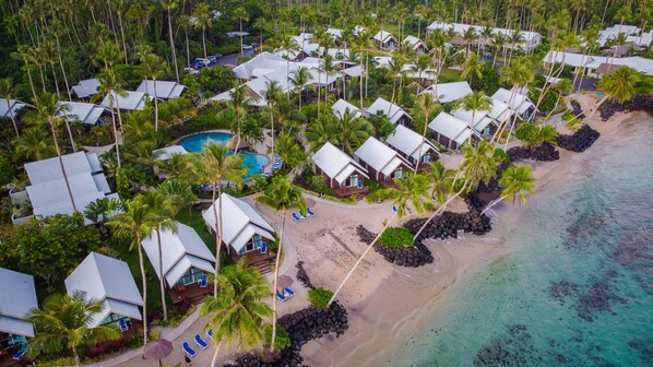 An aerial view of a resort with multiple bungalow-style accommodations, a central pool, and a beach area with lounge chairs. - Saletoga Sands Resorts (Matatufu)