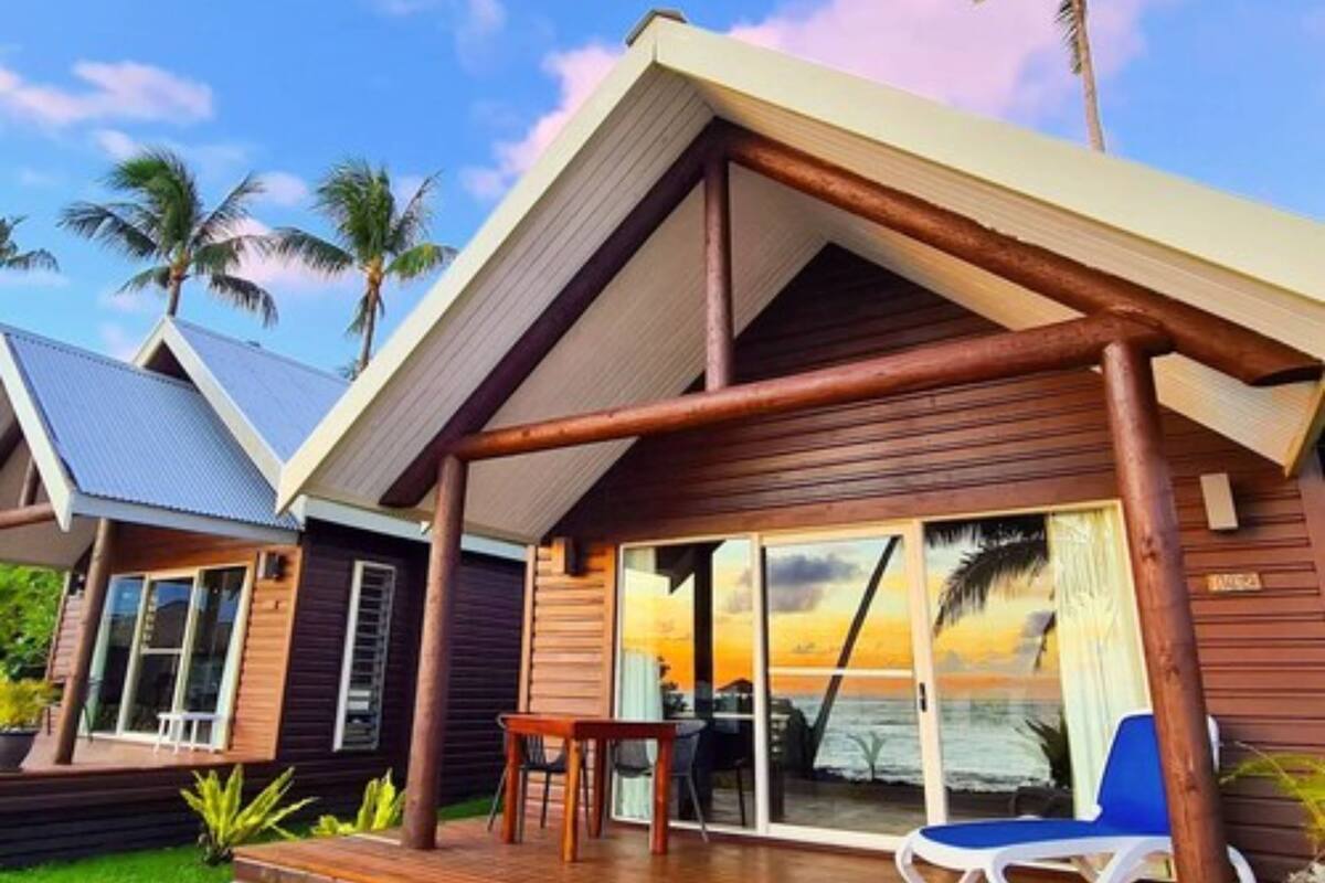A wooden cabin with a covered deck, large windows, and a view of the ocean.