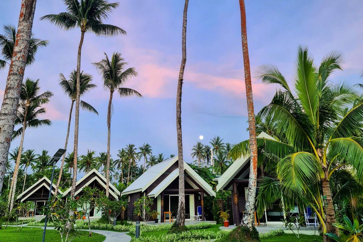 A resort with tall palm trees, a clear sky, and a building with a sloped roof.