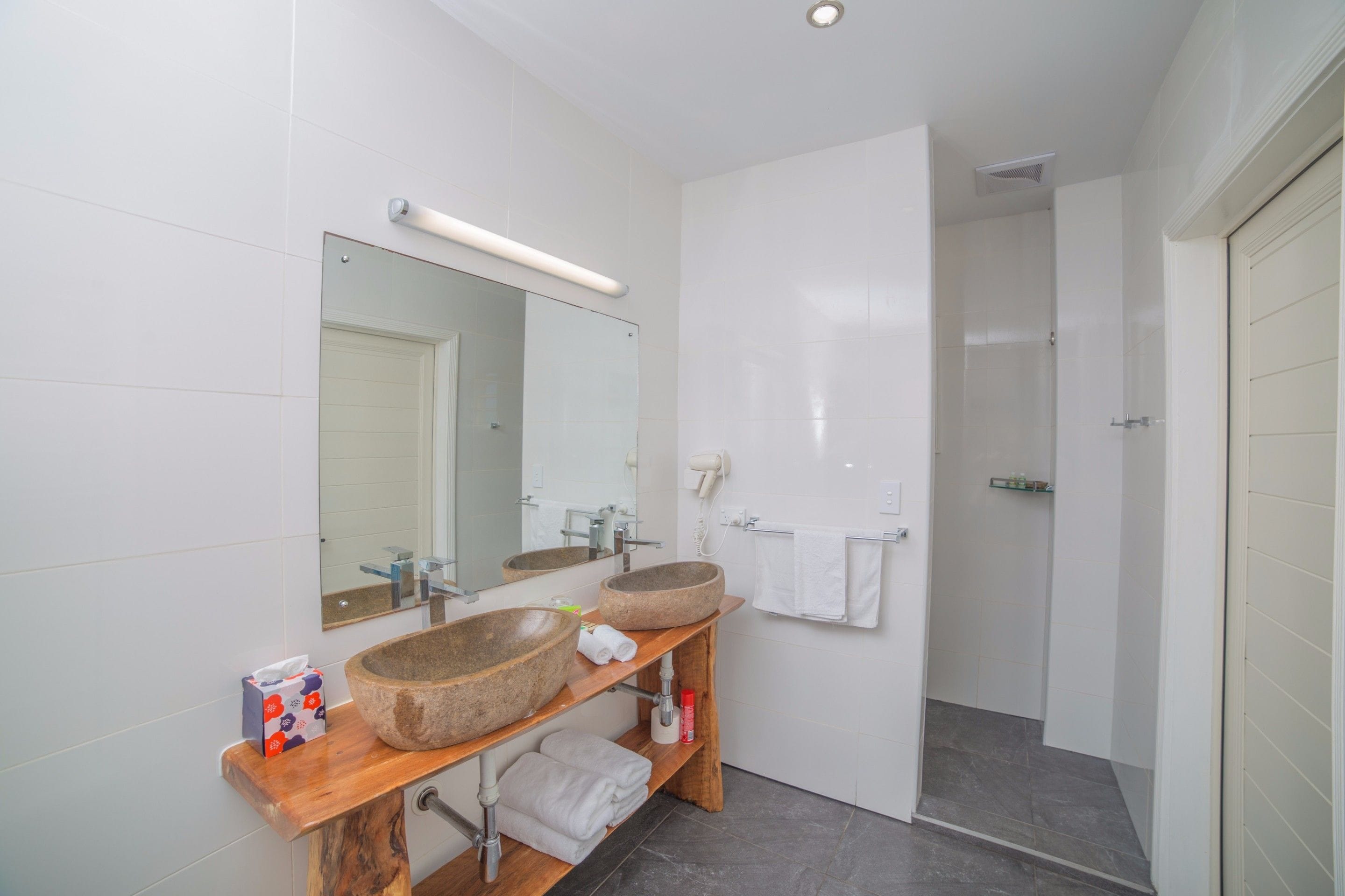 Une salle de bain moderne avec deux grands lavabos en pierre, un miroir et un espace douche.