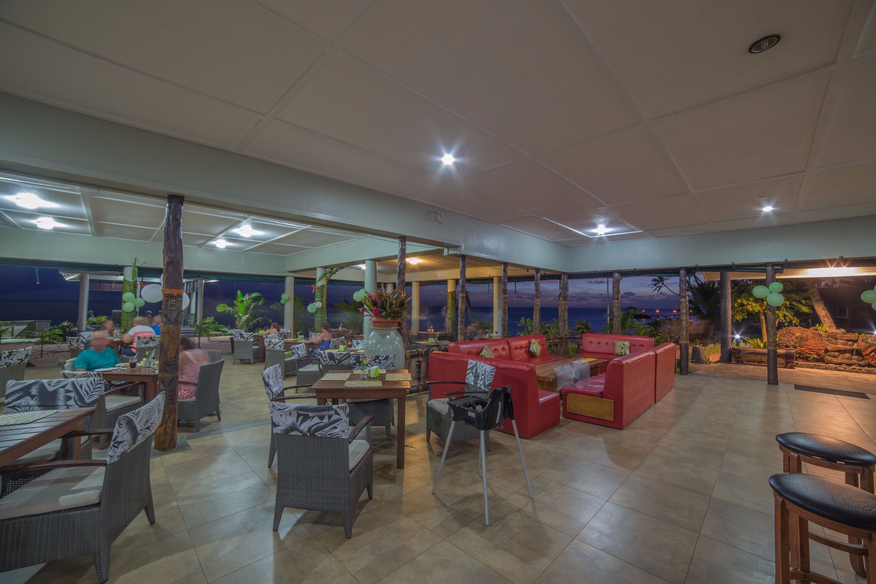 An outdoor restaurant with tables and chairs, a red sofa, and a view of the ocean.