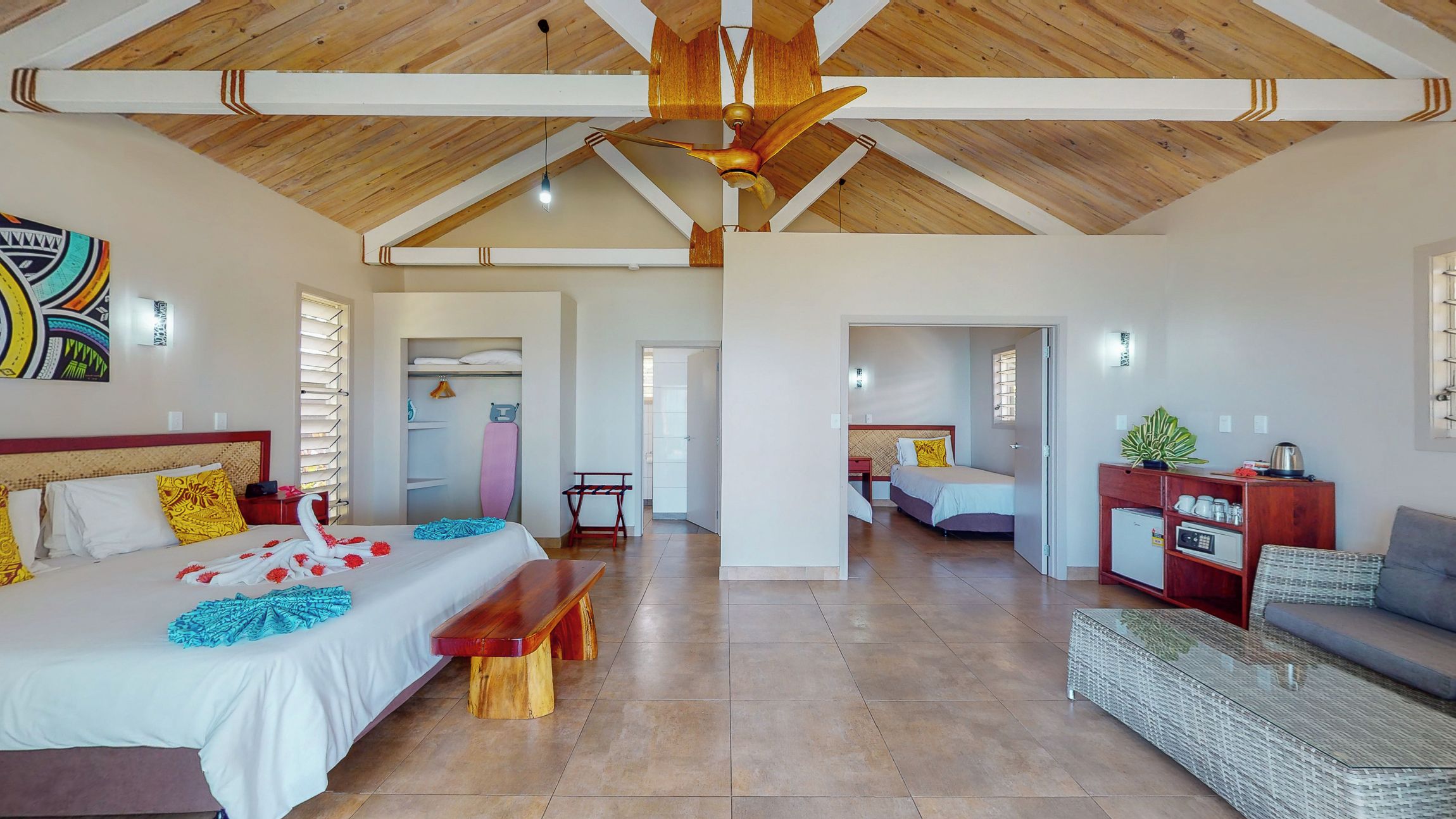 Una habitación amplia con techo alto, una cama con cabecera de madera, un banco, una mesita y un sofá.