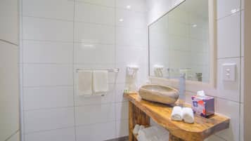 Un bagno moderno rivestito di piastrelle bianche, con un mobile lavabo in legno, un ampio specchio e cabina doccia in vetro.