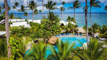 A resort with a pool surrounded by palm trees and a view of the ocean.