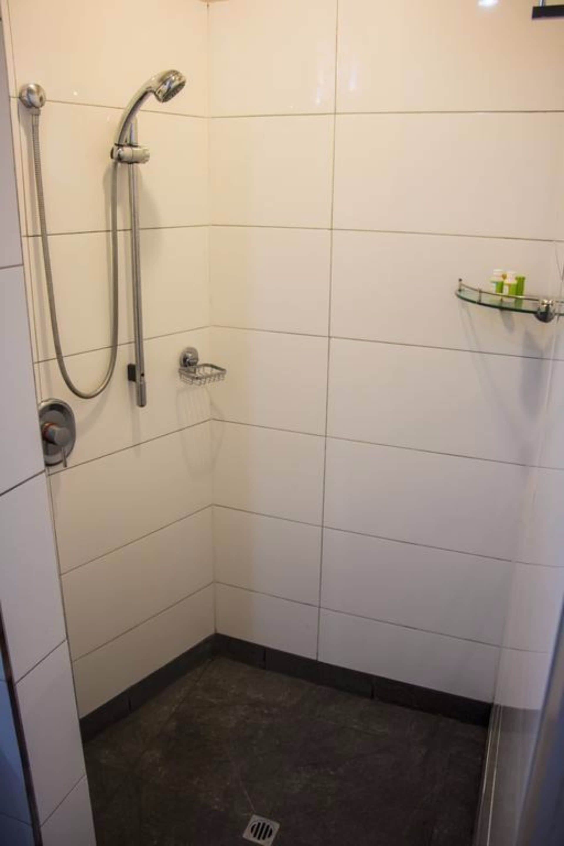 Un espacio de ducha pequeño con azulejos, un cabezal de ducha manual y un grifo instalado en la pared.