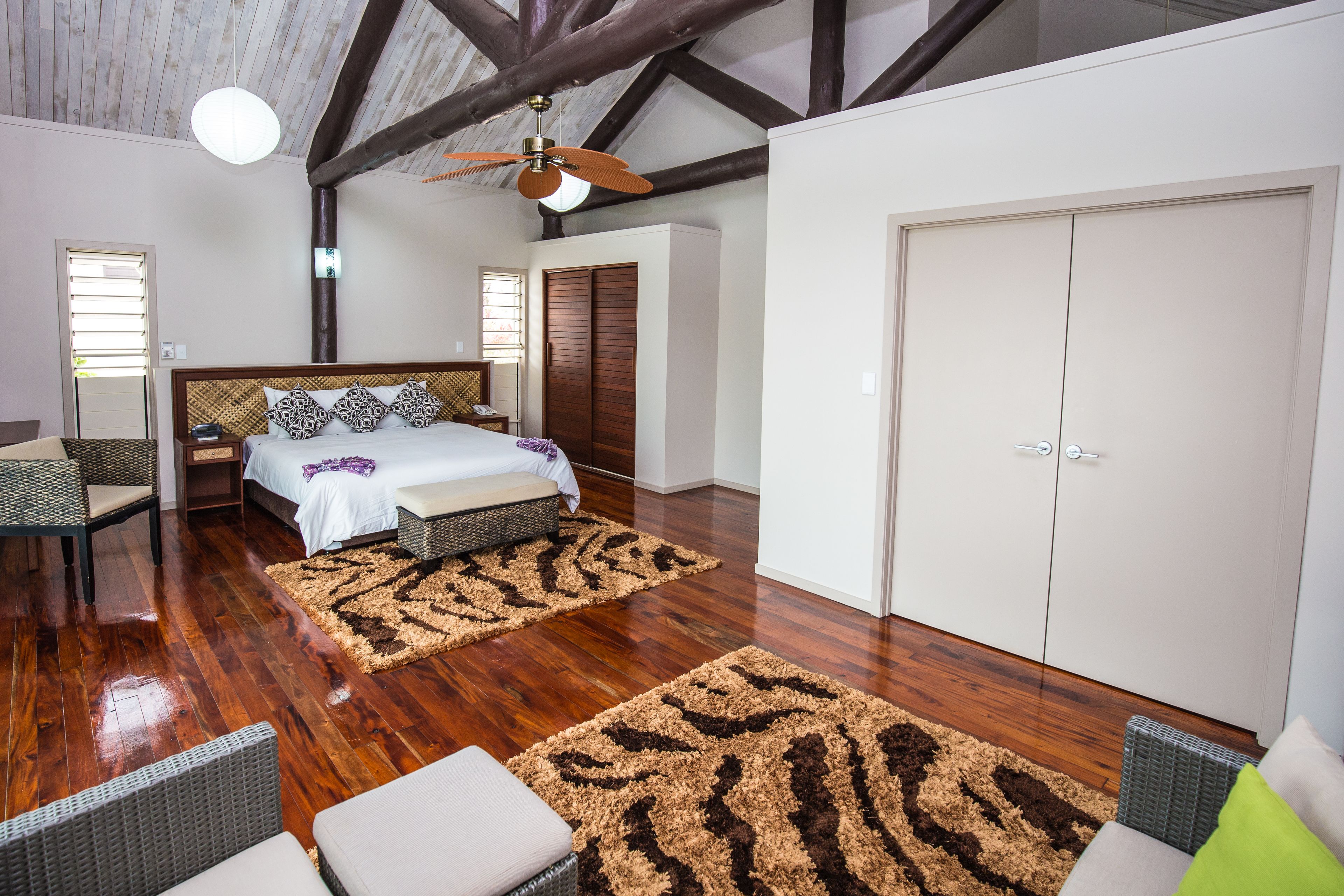 Un dormitorio con piso de madera, una cama con ropa de cama estampada, un ventilador de techo y un armario.