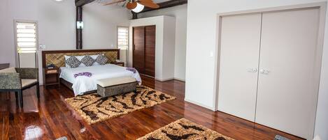 Un dormitorio con piso de madera, una cama con ropa de cama estampada, un ventilador de techo y un armario.
