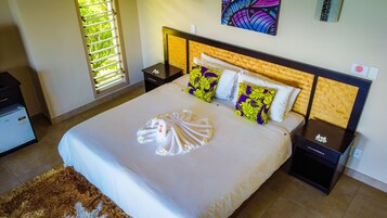 Una habitación de hotel con una cama grande, cabecera de madera, mesita de noche, escritorio y ventana con persianas.