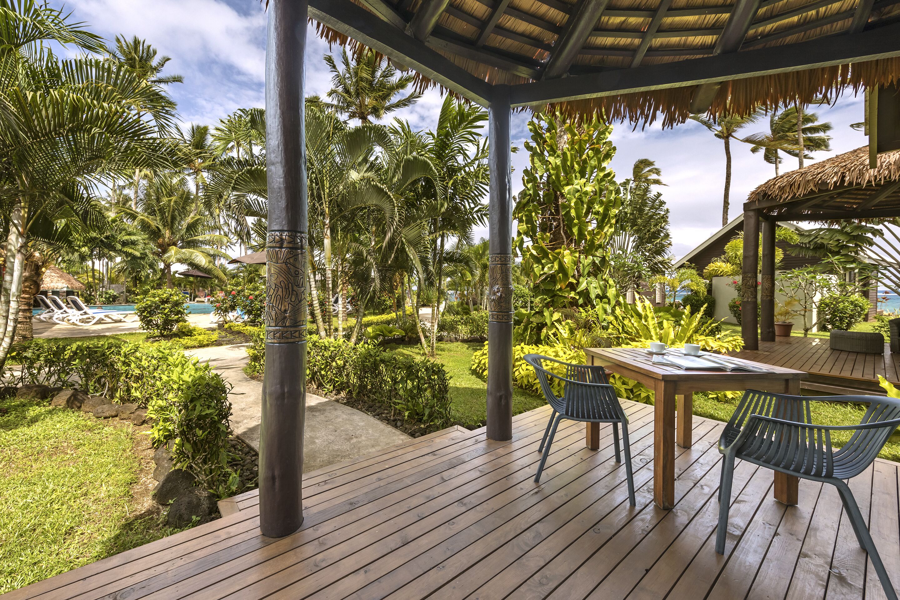 A wooden deck with a table and chairs, surrounded by lush greenery and palm trees.