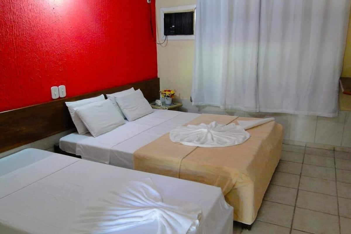 A hotel room with two beds, a red wall, a window with curtains, and a small table with a vase.