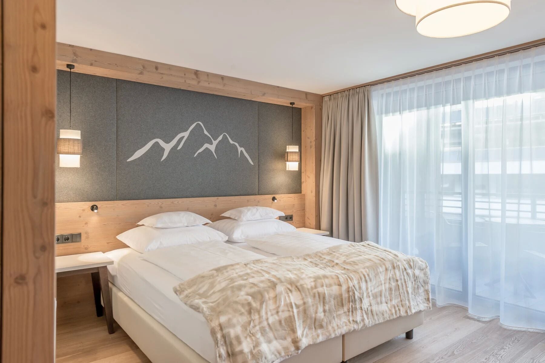 Una camera d'albergo moderna con un letto grande, una testiera in legno e un motivo a tema montagna sulla parete.