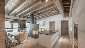 A modern kitchen with a central island, a dining area with a table and chairs, and a fireplace. - Hotel Gurglhof (Soelden)