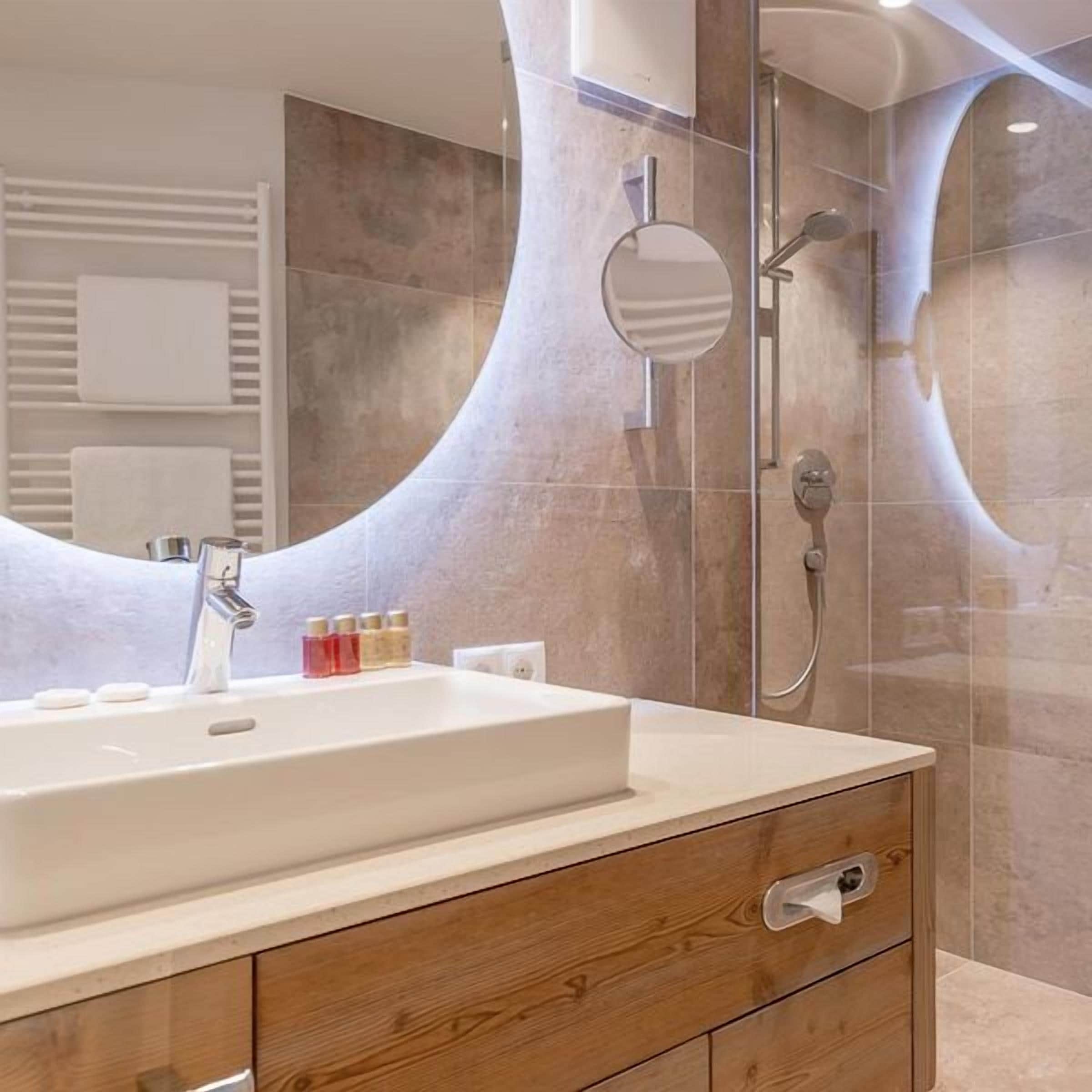 Un baño moderno con un lavamanos grande, tocador de madera y cabina de ducha de vidrio.