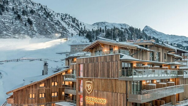 A multi-story wooden building with balconies, a check-in area, and a mountain backdrop. - Hotel Gurglhof (Soelden)