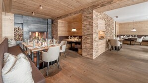 A modern interior with a wooden ceiling, a fireplace, and a dining area with white furniture. - Hotel Gurglhof (Soelden)