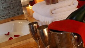 A spa room with a bathtub, candles, a stack of towels, and two champagne flutes on a table. - Fallen Angel (Cusco)