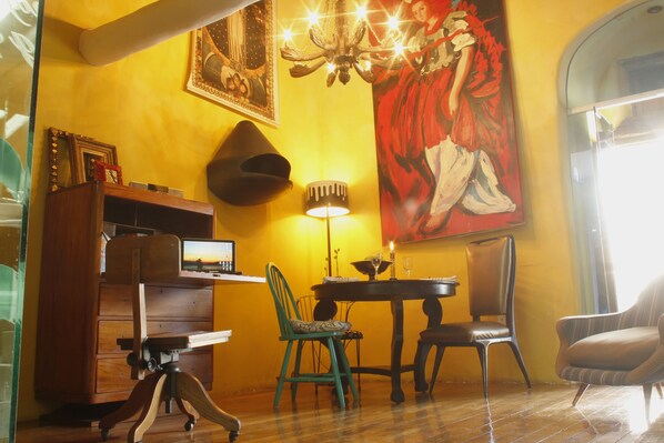 A dining area with a table, chairs, a chandelier, and a large painting on the wall.