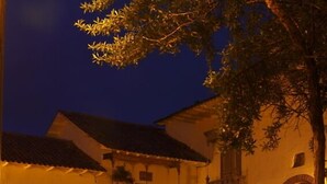 A courtyard with a bench, a building with a blue-lit entrance, and a tree. - Fallen Angel (Cusco)