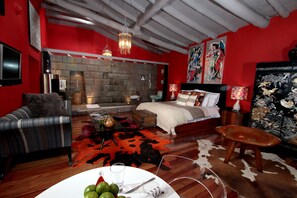 A modern bedroom with a stone fireplace, a bed with a white headboard, a leather sofa, and a red accent wall.