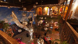A room with a large winged sculpture, a mural, and various decorative items. - Fallen Angel (Cusco)